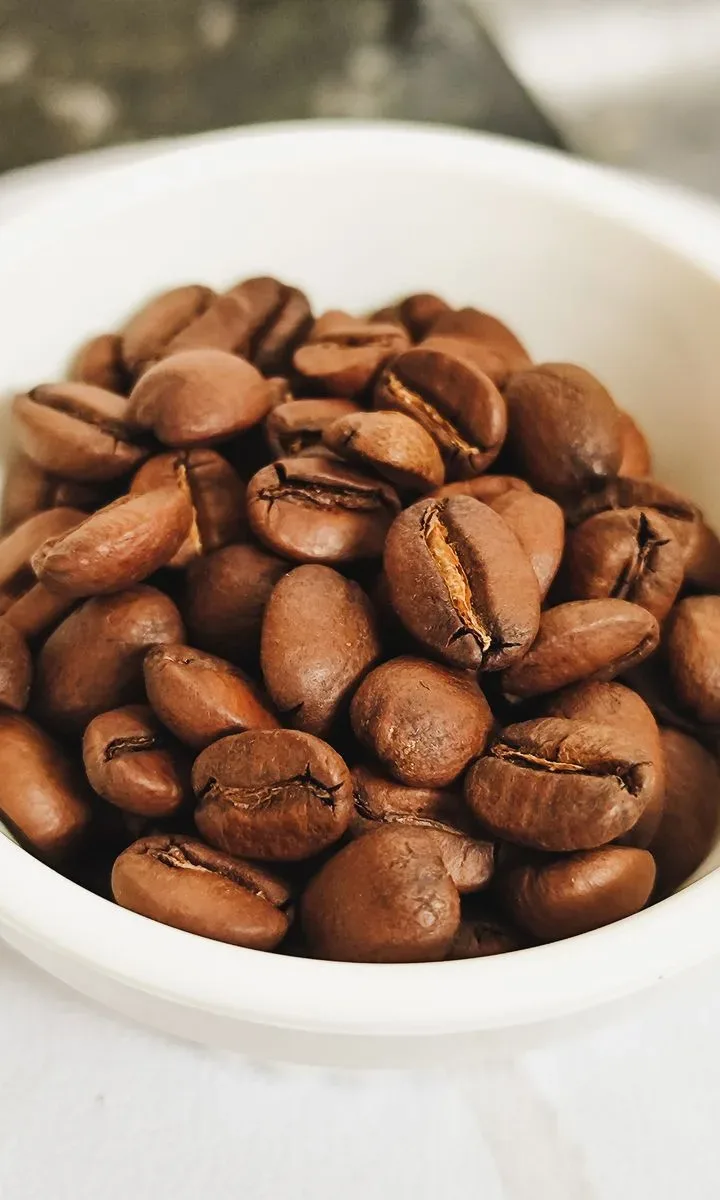 Cómo quitar olor a humedad en casa en pocos paso: 6 trucos naturales y caseros Un tazón lleno de granos de café colocados en una encimera de cocina, ilustrando el truco natural número 1 para absorber el olor a humedad.