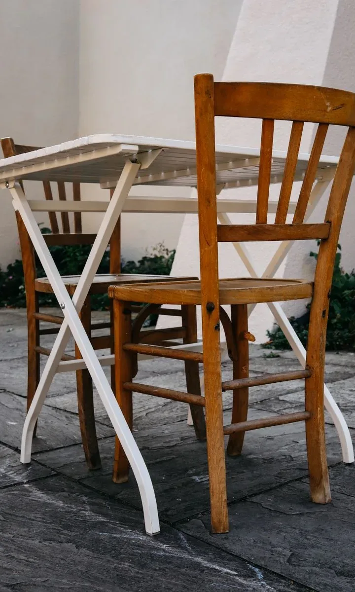Una mesa de comedor extensible colocada contra la pared en un departamento pequeño, con sillas apilables y una lámpara colgante sobre ella.