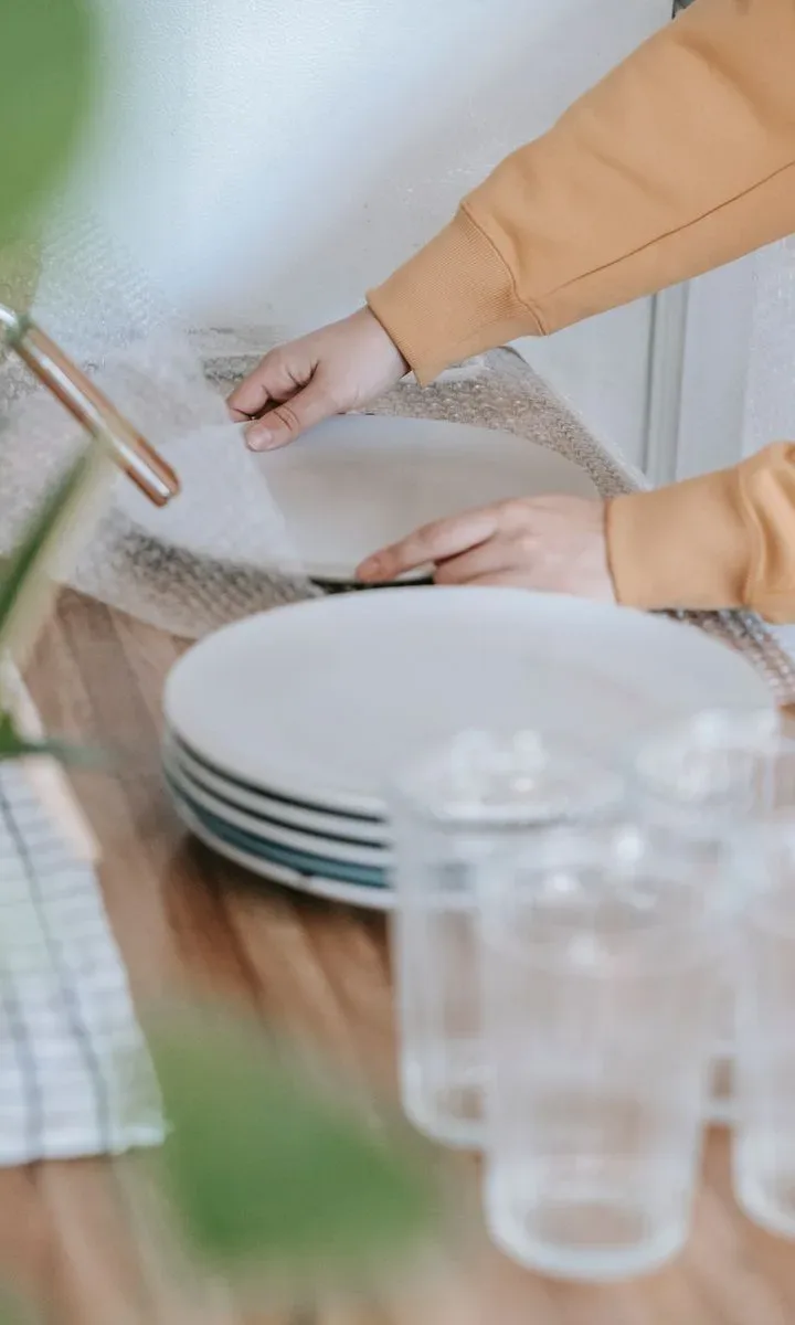 Qué limpiar cada día para evitar el caos en espacios pequeños. Persona limpiando y organizando la encimera de una cocina pequeña con productos de limpieza y utensilios colocados en su lugar.
