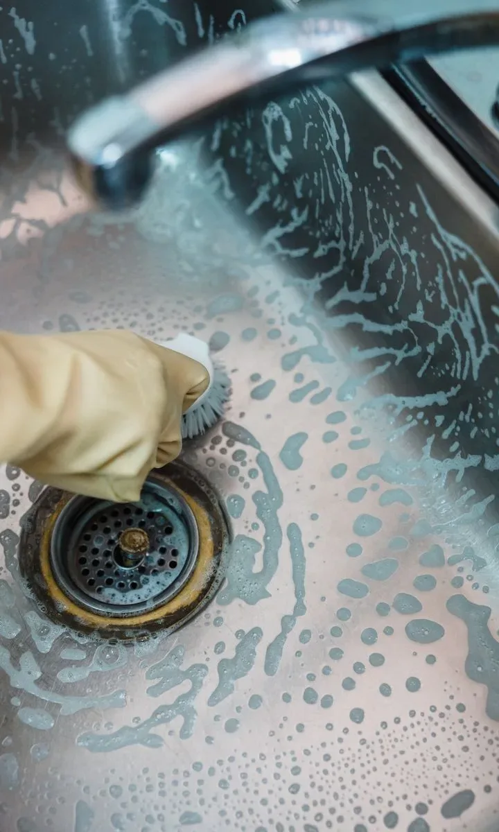 Cómo quitar olor a humedad en casa en pocos paso: 6 trucos naturales y caseros Vertiendo bicarbonato de sodio y vinagre en un desagüe de lavabo para eliminar el mal olor y la humedad, mostrando un método casero eficaz.