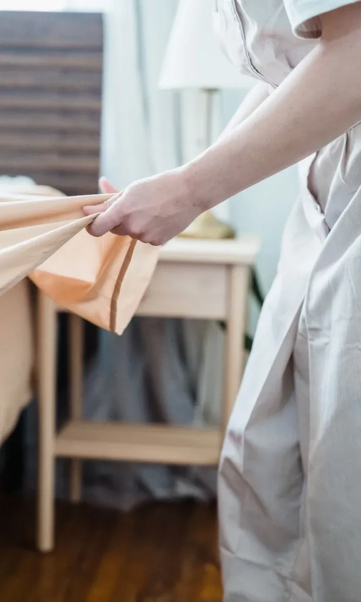 La rutina de limpieza de los domingos para empezar bien la semana. Manos colocando sábanas limpias sobre una cama, mostrando la tarea de lavar y cambiar las sábanas los domingos según los expertos.