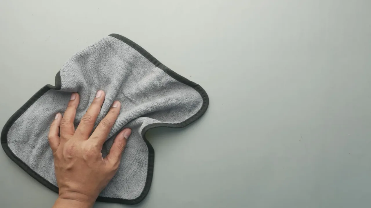 Cómo limpiar vidrios sin dejar marcas usando productos económicos Mano limpiando un espejo con papel periódico en movimientos en S, técnica profesional para evitar marcas.