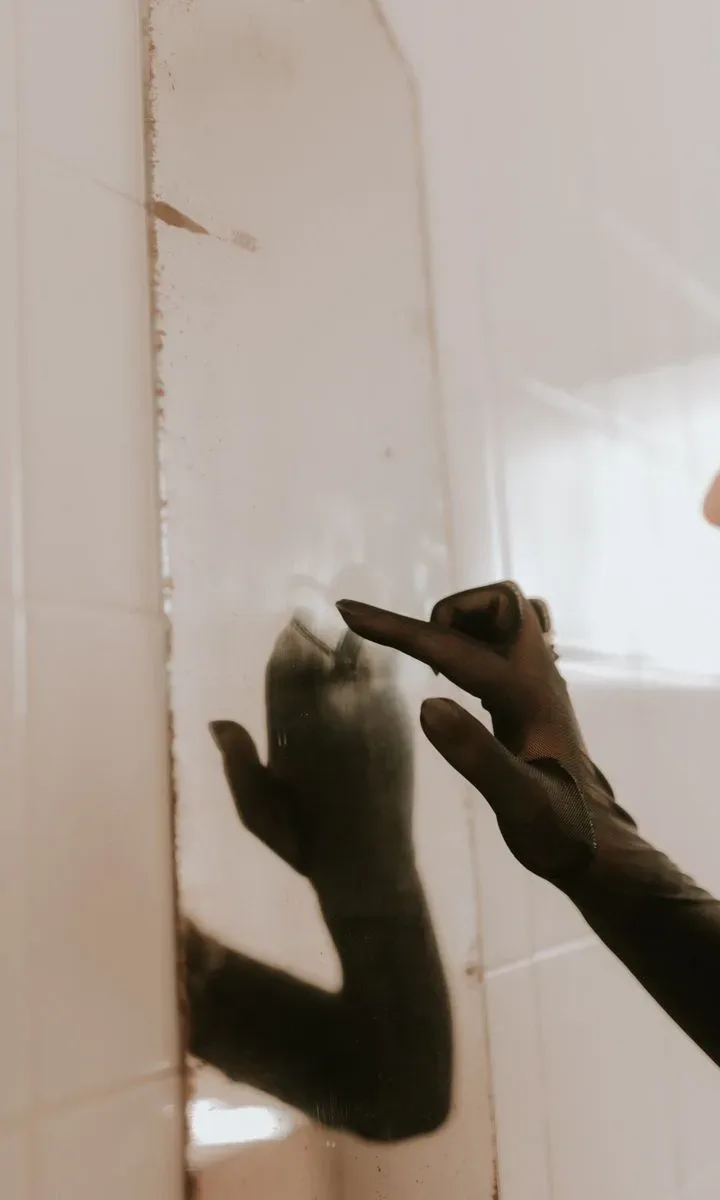 Cómo evitar que tu casa parezca desordenada y sucia Persona limpiando un espejo de baño con un paño, mostrando cómo mantener el baño limpio y reluciente.