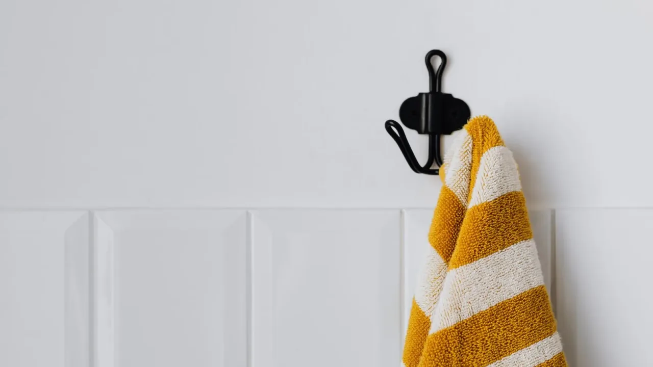 Colgadores adhesivos en la pared del baño sujetando escobillas y paños de limpieza, maximizando el espacio vertical.