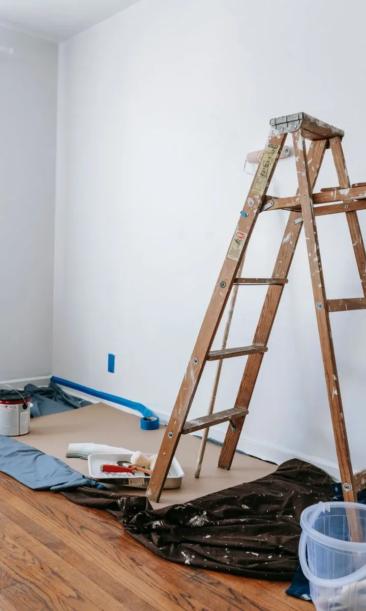 Una mano con un paño y producto limpiador retirando manchas de pintura blanca de un suelo de madera después de una reforma.
