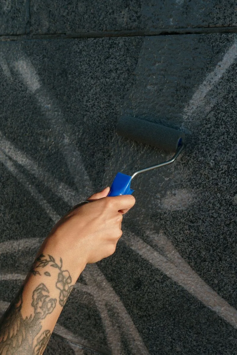 Cómo quitar manchas difíciles de paredes pintadas Una persona limpia una mancha en una pared pintada de color claro con una esponja y un balde de agua.